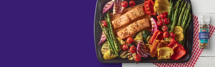 Sheet pan filled with grilled vegetables and salmon portions with garlic pepper seasoning on the side