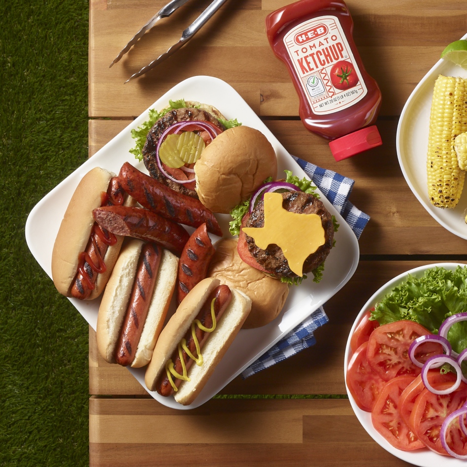 Hot dogs. burgers, ketchup, corn, and sliced veggies