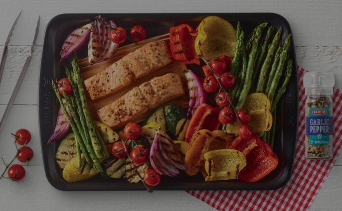 Sheet pan filled with grilled vegetables and salmon portions with garlic pepper seasoning on the side