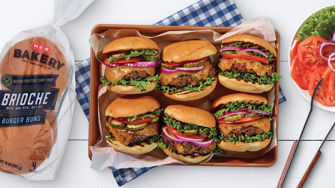 Multiple hamburgers on a serving tray next to a package of H‑E‑B brioche burger buns
