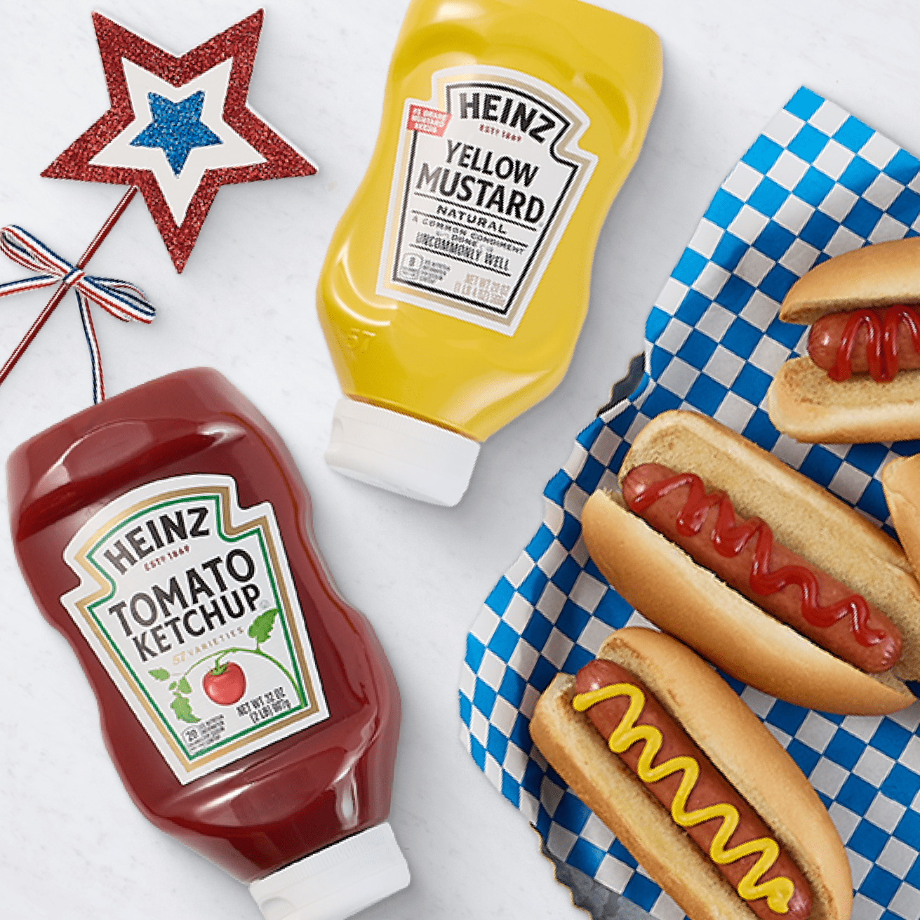 Heinz ketchup and mustard bottles with hot dogs on a checkered tray, decorated with patriotic star and ribbon.