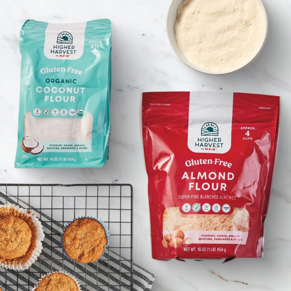 Higher Harvest by H‑E‑B Gluten-Free Organic Coconut and Almond Flour bags, a bowl of flour, and baked muffins on a cooling rack.