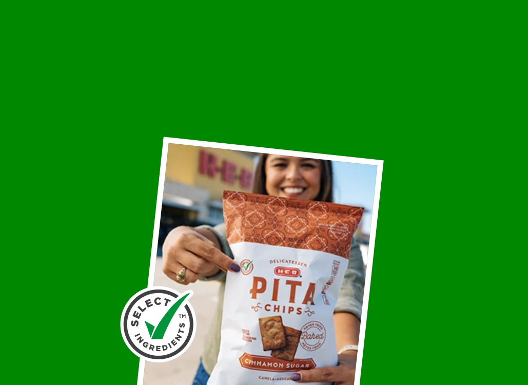 A girl pointing to the green checkmark on a bag of H‑E‑B Select Ingredients Pita Chips