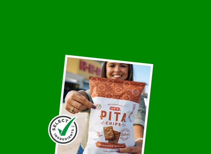 A girl pointing to the green checkmark on a bag of H‑E‑B Select Ingredients Pita Chips
