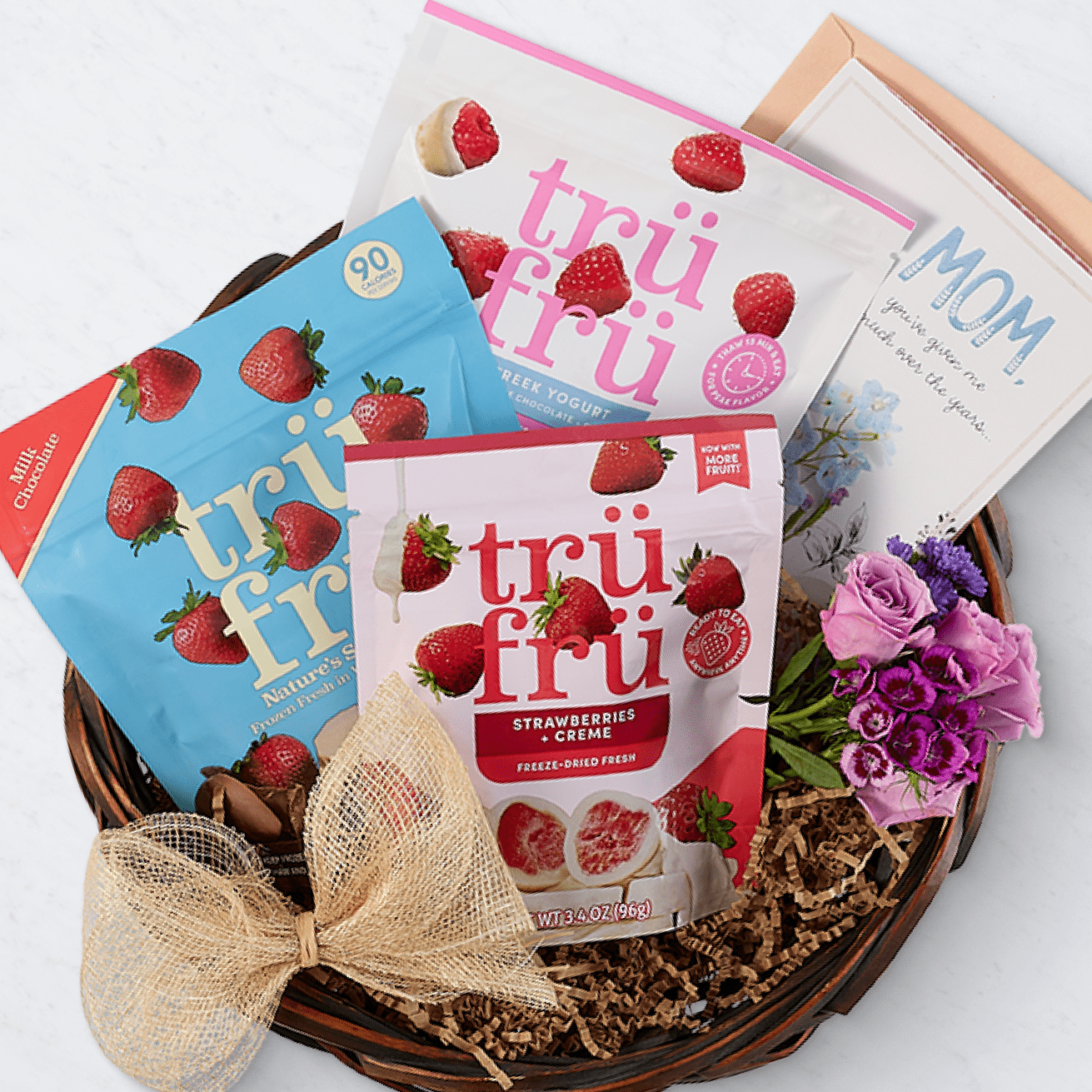Gift basket featuring Tru Fru freeze-dried strawberries and creme snacks, a "Mom" greeting card, and a bouquet of pink and purple flowers.