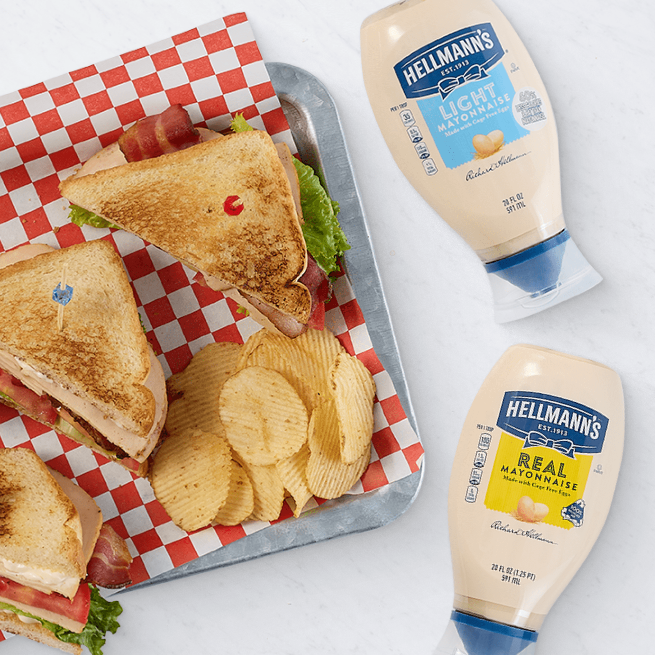 Tray with club sandwiches and potato chips on red and white checkered paper, featuring Hellmann's Light Mayonnaise and Real Mayonnaise bottles.