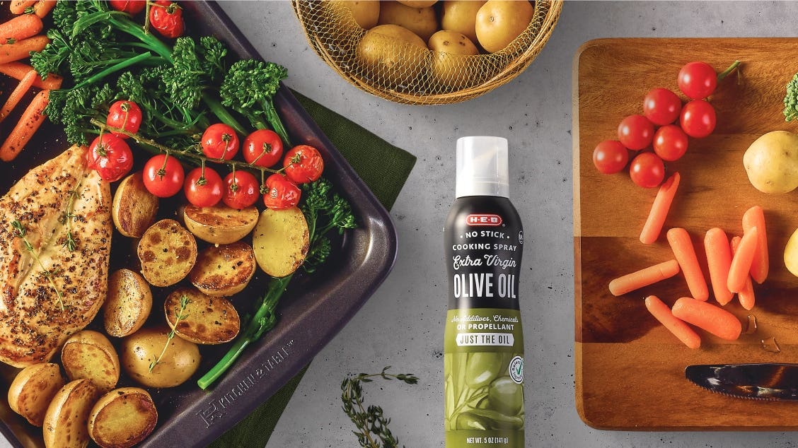 H‑E‑B Extra Virgin Olive Oil No-Stick Cooking Spray alongside a one pan meal of baked chicken, potatoes, broccoli florets, onions, and carrots.