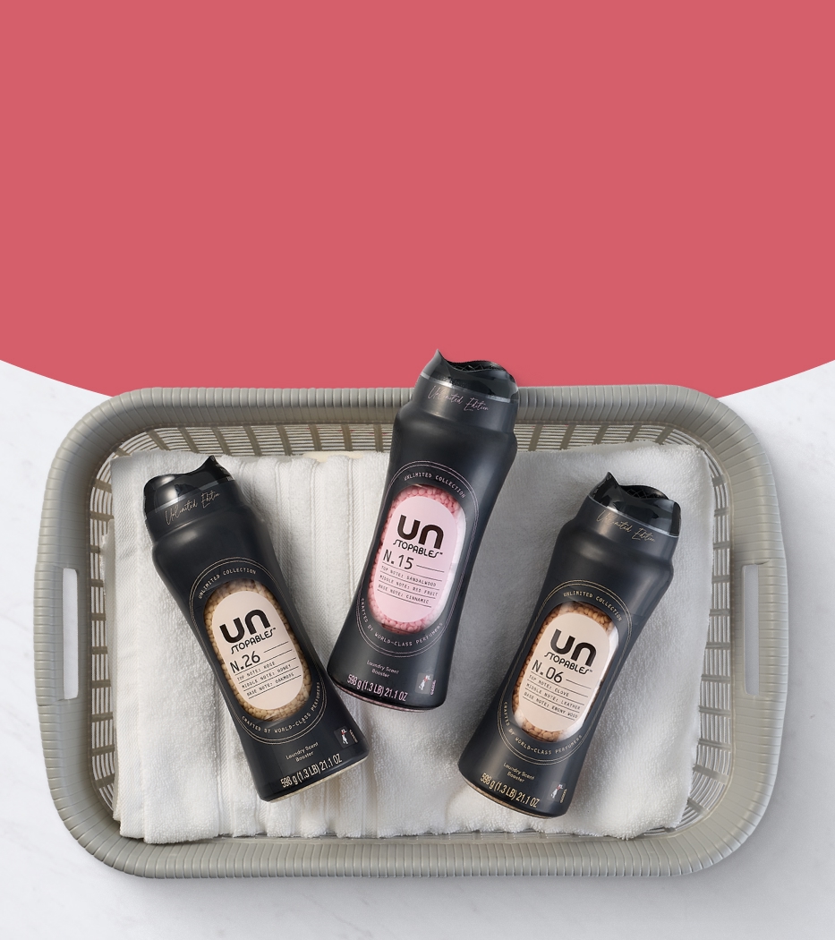 Three bottles of Unstoppable laundry scent boosters in a basket with white towels, set against a pink and white background. 