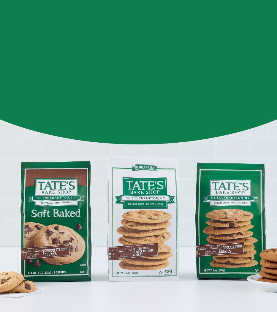 Three varieties of Tate's Bake Shop cookies, including Soft Baked Chocolate Chip, displayed on a white counter with a glass of milk and a green background.