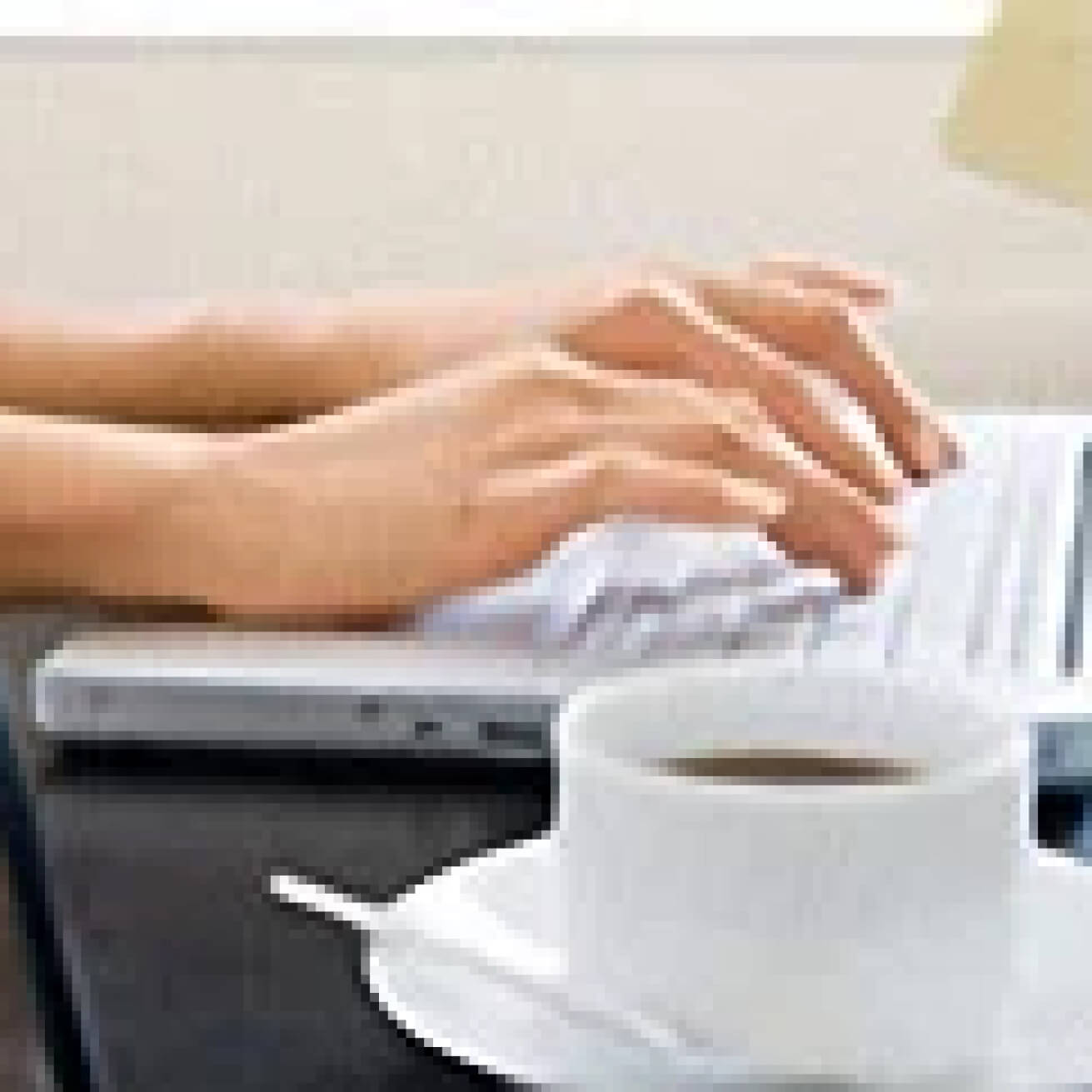 Hands typing on a keyboard and a coffee cup