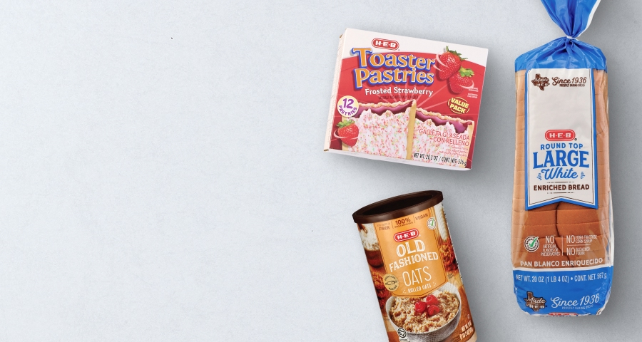 A selection of H‑E‑B branded snacks including potato chips, tortilla chips, and pretzels displayed on a wooden surface with a light background.