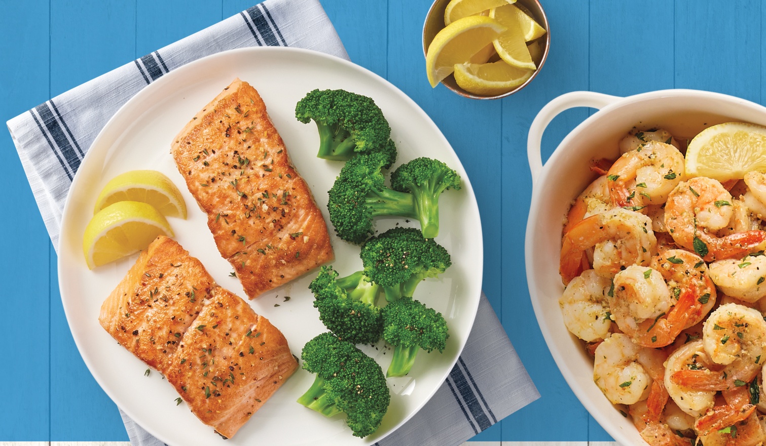 A plate with salmon, lemons, and broccoli; a bowl of shrimp and lemon