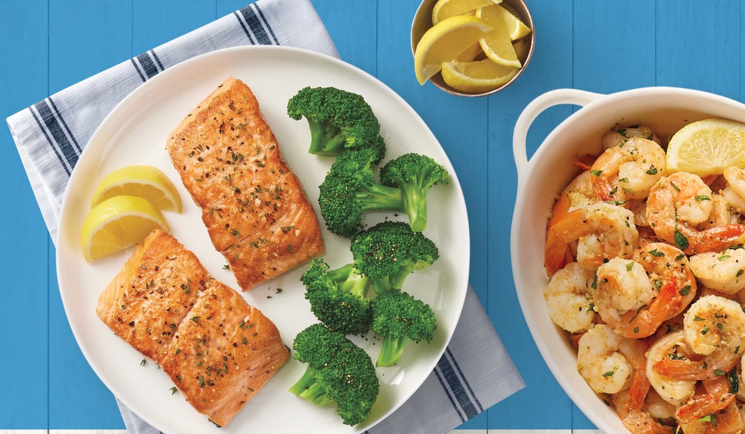 A plate with salmon, lemons, and broccoli; a bowl of shrimp and lemon