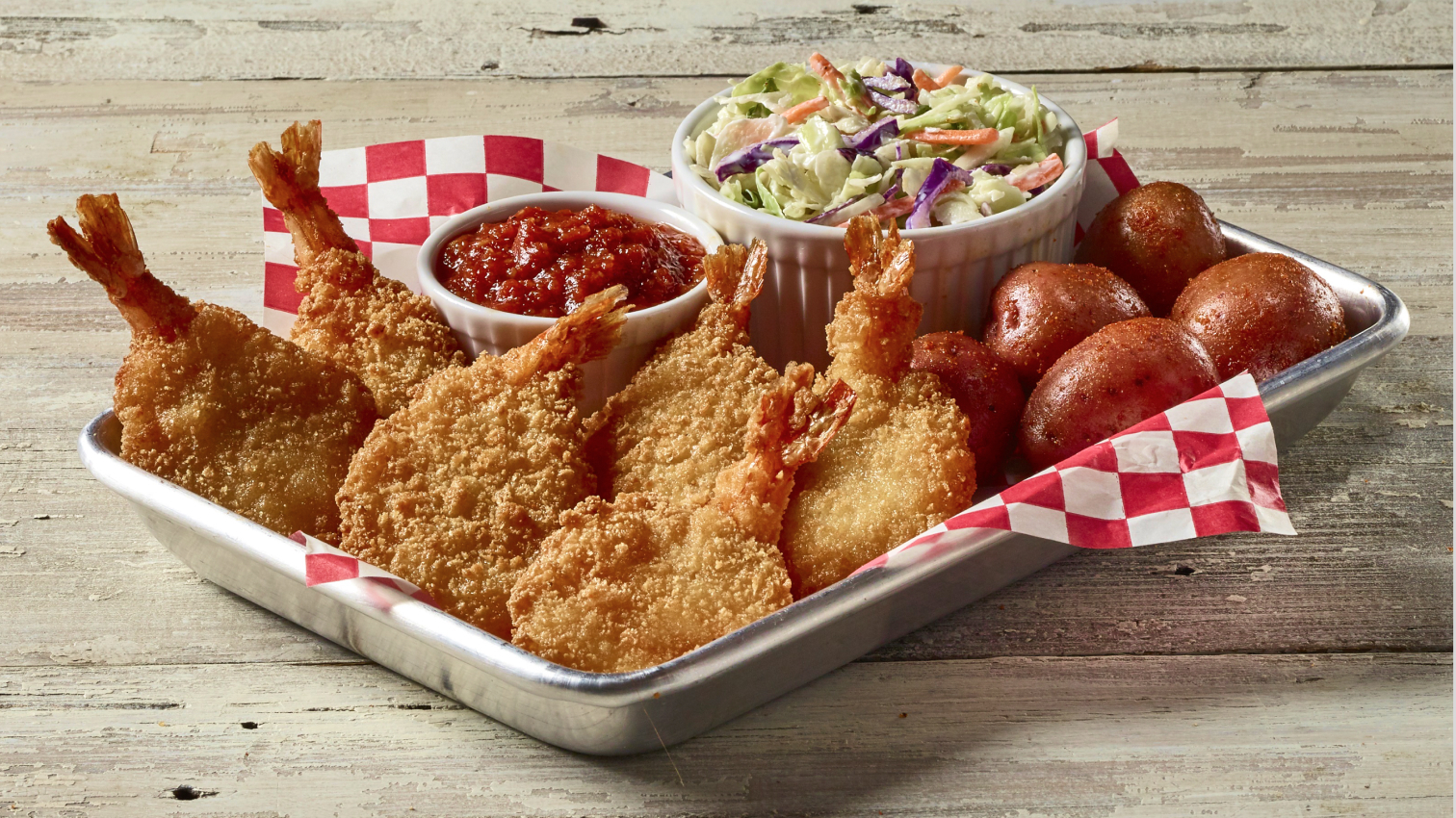 Fried shrimp, potatoes, cole slaw, and a sauce on a tray with red checkered paper lining 