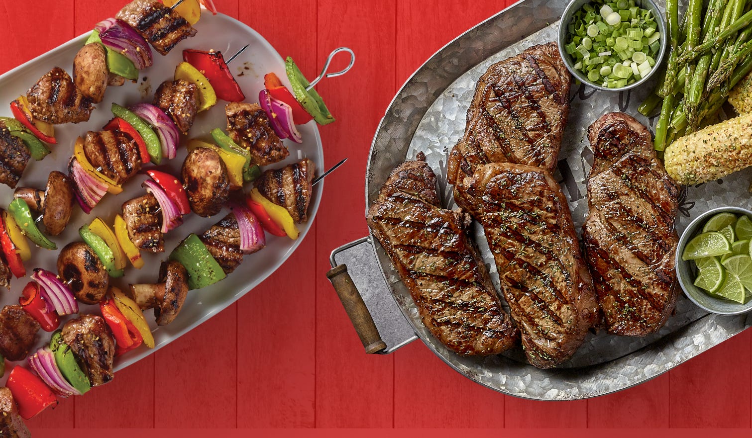 A plate of steak kabobs and steaks with corn, asparagus, lime, and chopped green onions