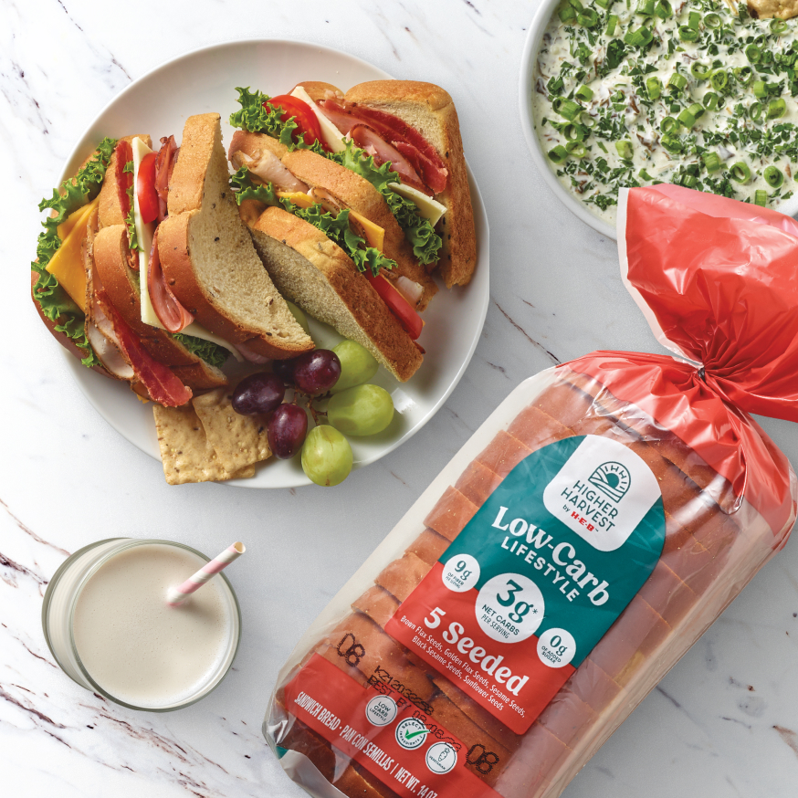 Higher Harvest by H‑E‑B Low Carb Lifestyle 5 Seeded Bread next to a sandwich, glass of milk, and a dip